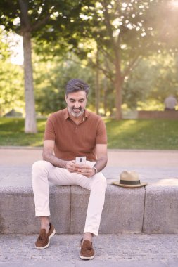 Parkta dışarıda cep telefonu kullanan bir adam dinleniyor. Teknoloji konsepti.