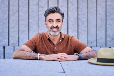 Orta yaşlı bir adamın fotoğrafı. Kameraya bakıyor ve dışarıda gülümsüyor..