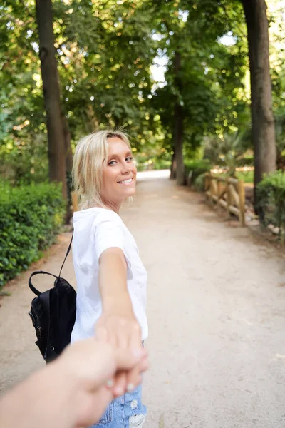 手を取りながらカメラと笑顔を見ている若い女性と公園の屋外散歩に誰かをリード — ストック写真