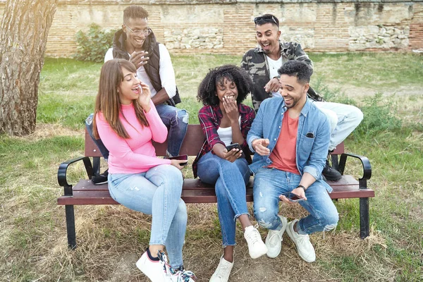 屋外のベンチに座って携帯電話を使用している間 楽しさと笑顔を持つ多民族の友人 テクノロジーと友情の概念 — ストック写真