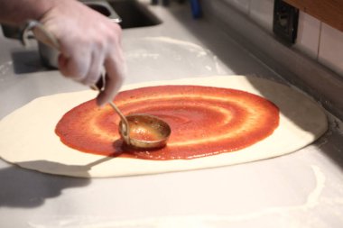 Pizza şefi ticari bir mutfakta sosu tabana koydu.