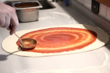 Pizza şefi ticari bir mutfakta sosu tabana koydu.