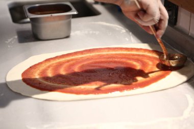 Pizza şefi ticari bir mutfakta sosu tabana koydu.