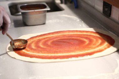 Pizza şefi ticari bir mutfakta sosu tabana koydu.