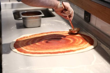 Pizza şefi ticari bir mutfakta sosu tabana koydu.