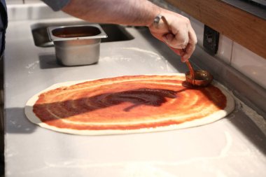 Pizza şefi ticari bir mutfakta sosu tabana koydu.