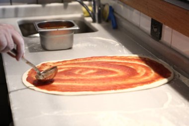 Pizza şefi ticari bir mutfakta sosu tabana koydu.