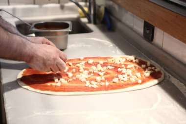 Pizza şefi ticari bir mutfakta sosu tabana koydu.