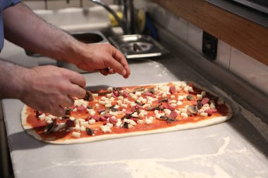 Pizza şefi ticari bir mutfakta sosu tabana koydu.