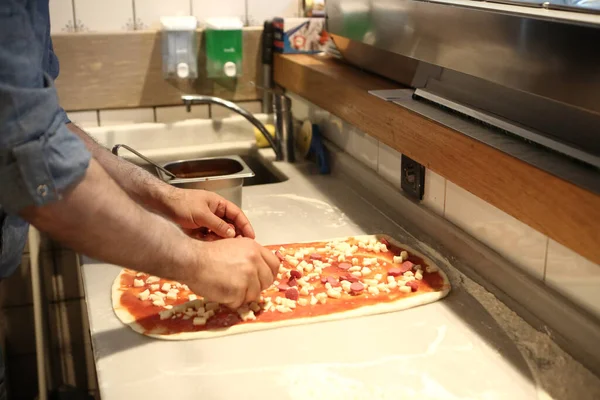 Pizza şefi ticari bir mutfakta sosu tabana koydu.