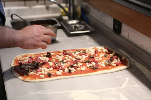 Pizza şefi ticari bir mutfakta sosu tabana koydu.