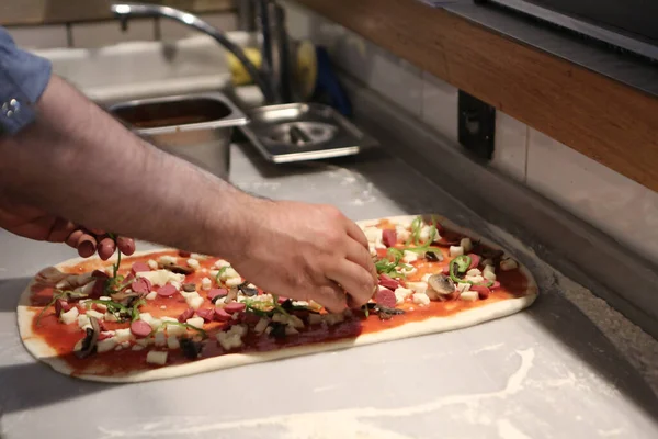 Pizza şefi ticari bir mutfakta sosu tabana koydu.