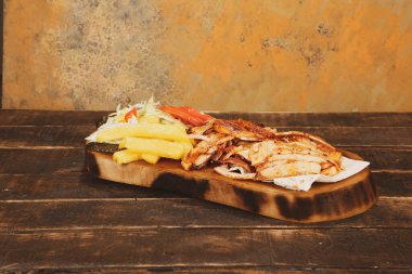 Doner kebabı kesme tahtasının üzerinde duruyor. Et, soğan ve salata ile Shawarma eski ve karanlık bir tahta masada yatıyor.