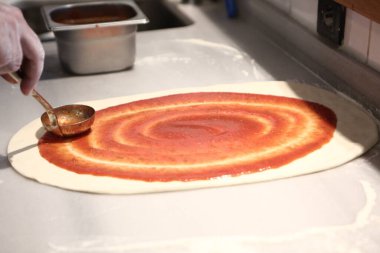 Pizza şefi ticari bir mutfakta sosu tabana koydu.