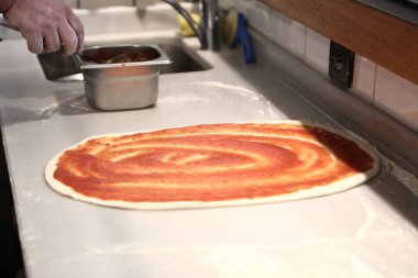 Pizza şefi ticari bir mutfakta sosu tabana koydu.