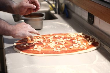 Pizza şefi ticari bir mutfakta sosu tabana koydu.