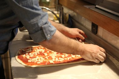 Pizza şefi ticari bir mutfakta sosu tabana koydu.