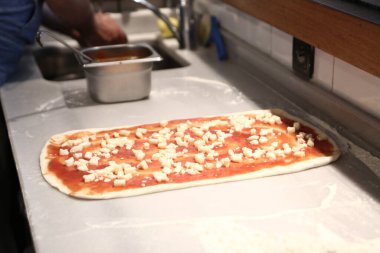 Pizza şefi ticari bir mutfakta sosu tabana koydu.