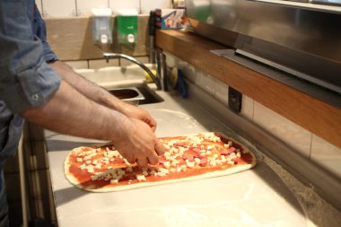 Pizza şefi ticari bir mutfakta sosu tabana koydu.