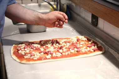 Pizza şefi ticari bir mutfakta sosu tabana koydu.