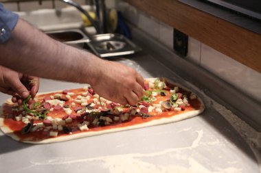 Pizza şefi ticari bir mutfakta sosu tabana koydu.