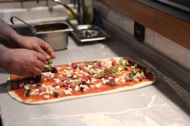 Pizza şefi ticari bir mutfakta sosu tabana koydu.