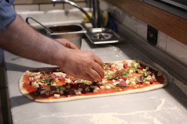 Pizza şefi ticari bir mutfakta sosu tabana koydu.