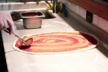 Pizza şefi ticari bir mutfakta sosu tabana koydu.