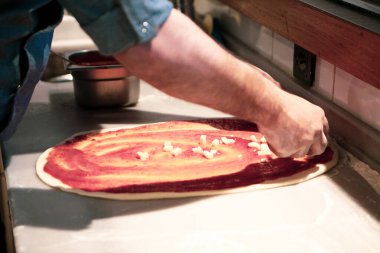 Pizza şefi ticari bir mutfakta sosu tabana koydu.