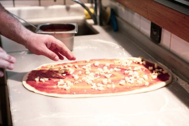 Pizza şefi ticari bir mutfakta sosu tabana koydu.