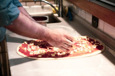 Pizza şefi ticari bir mutfakta sosu tabana koydu.