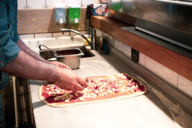 Pizza şefi ticari bir mutfakta sosu tabana koydu.