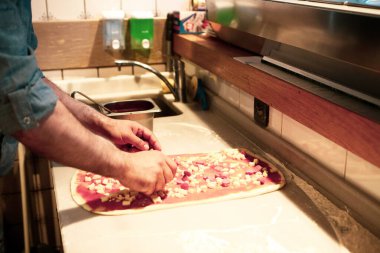 Pizza şefi ticari bir mutfakta sosu tabana koydu.