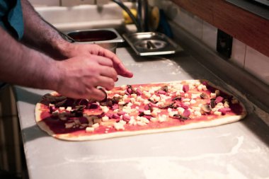 Pizza şefi ticari bir mutfakta sosu tabana koydu.