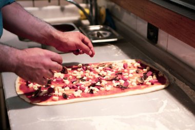 Pizza şefi ticari bir mutfakta sosu tabana koydu.