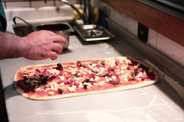 Pizza şefi ticari bir mutfakta sosu tabana koydu.