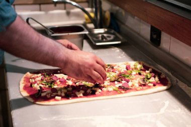 Pizza şefi ticari bir mutfakta sosu tabana koydu.