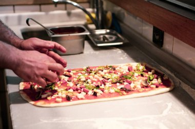 Pizza şefi ticari bir mutfakta sosu tabana koydu.