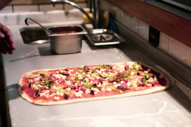 Pizza şefi ticari bir mutfakta sosu tabana koydu.