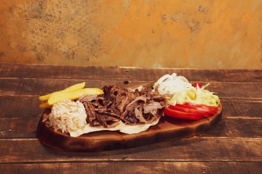 Doner kebabı kesme tahtasının üzerinde duruyor. Et, soğan ve salata ile Shawarma eski ve karanlık bir tahta masada yatıyor.