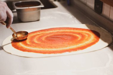Pizza şefi ticari bir mutfakta sosu tabana koydu.