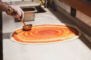 Pizza şefi ticari bir mutfakta sosu tabana koydu.