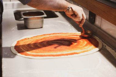 Pizza şefi ticari bir mutfakta sosu tabana koydu.