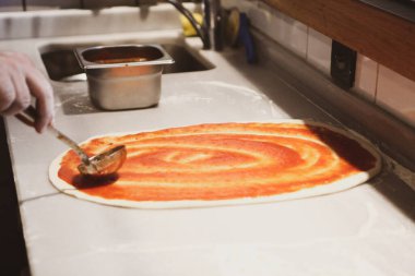 Pizza şefi ticari bir mutfakta sosu tabana koydu.