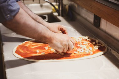 Pizza şefi ticari bir mutfakta sosu tabana koydu.