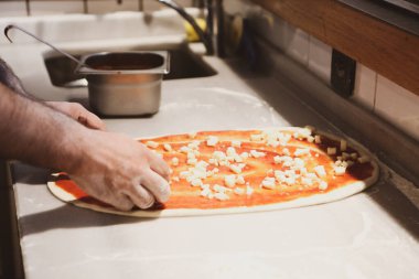 Pizza şefi ticari bir mutfakta sosu tabana koydu.