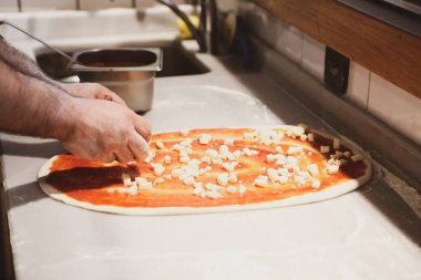 Pizza şefi ticari bir mutfakta sosu tabana koydu.
