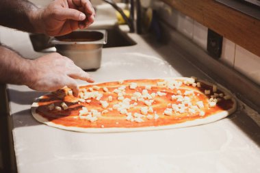 Pizza şefi ticari bir mutfakta sosu tabana koydu.