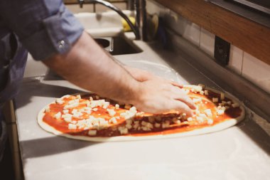 Pizza şefi ticari bir mutfakta sosu tabana koydu.