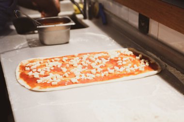 Pizza şefi ticari bir mutfakta sosu tabana koydu.